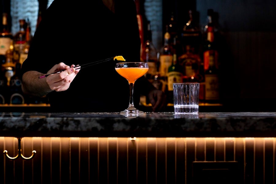 A bartender carefully garnishes a craft cocktail in a dimly lit, upscale bar.